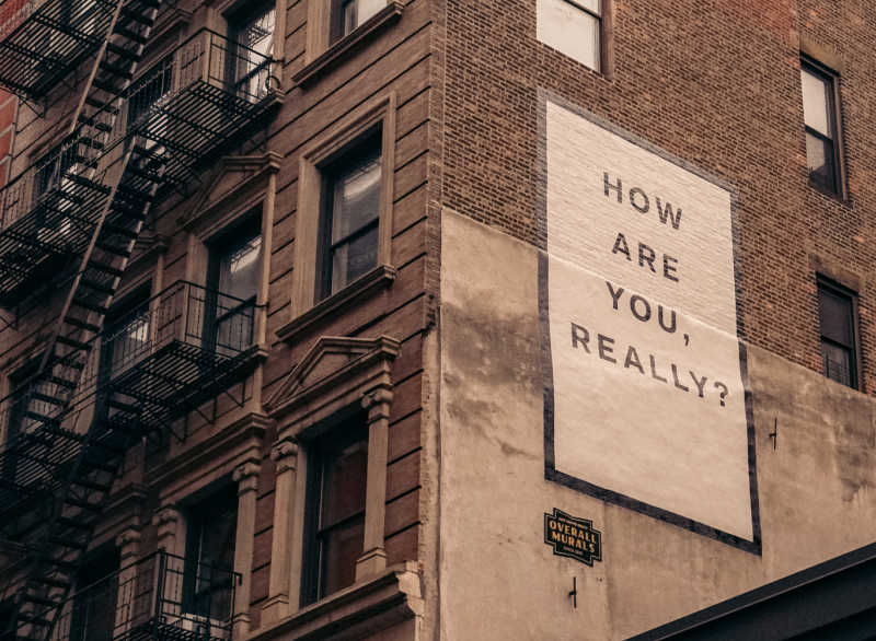 Large mural saying 'How are you really' on side of brownstone building