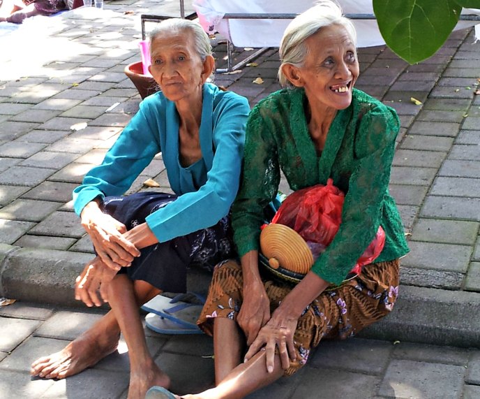 Two Balinese ladies sitting on the pavement watching the preparations for a cremation