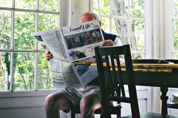 Grandfather sitting on chair reading newspaper entitled Good Life.  Photo by Sam Wheeler