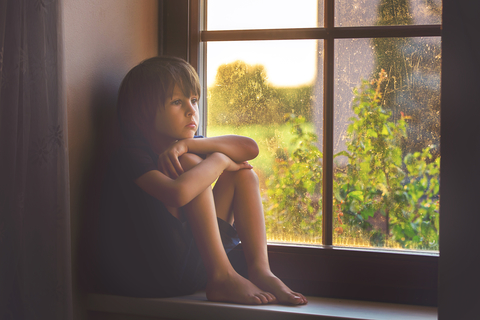 sad boy upset at finding out he is adopted. Staring out of the window of his room.